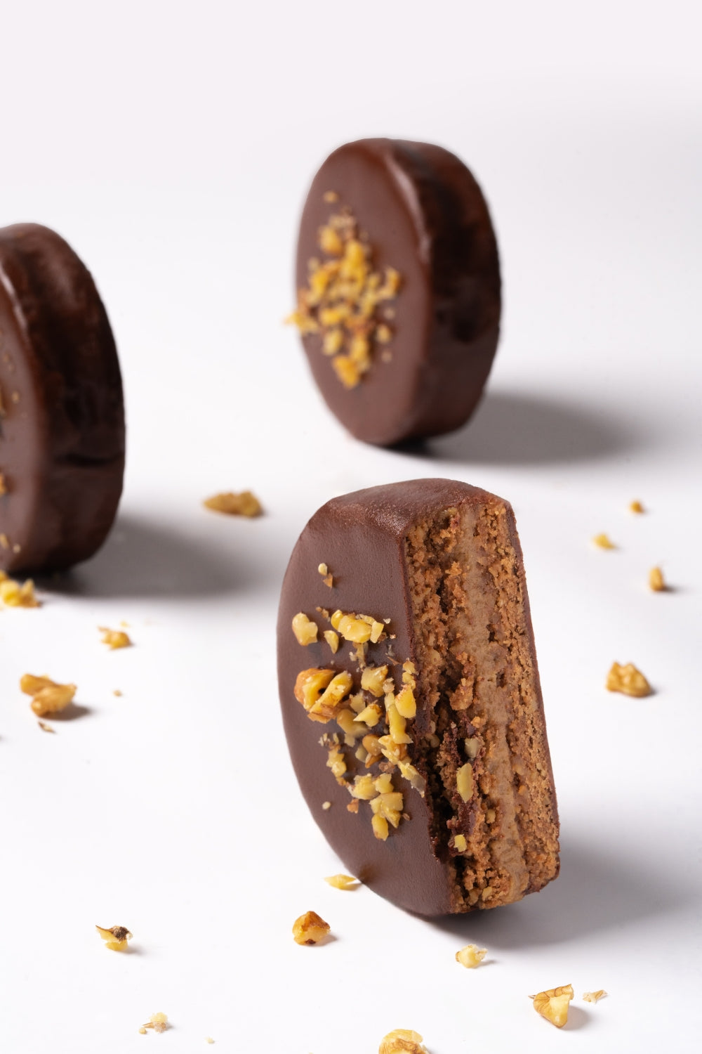 Tres alfajores de nueces sobre una superficie blanca. Uno está partido por la mitad.