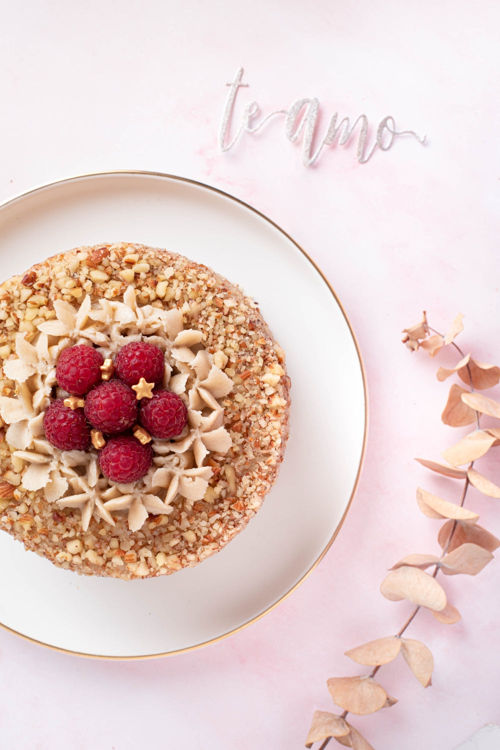 Mini torta de zanahoria en un plato color blanco sobre un fondo rosado pastel. Al lado de la torta hay un topper que dice "te amo".