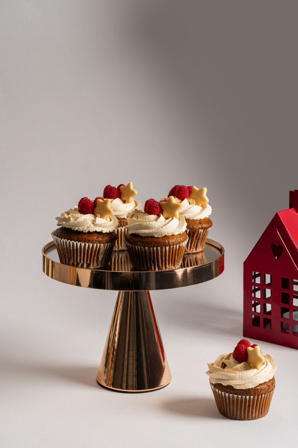 Un parante sostiene cuatro cupcakes de berries. Al lado en la mesa se encuentra otro cupcake.