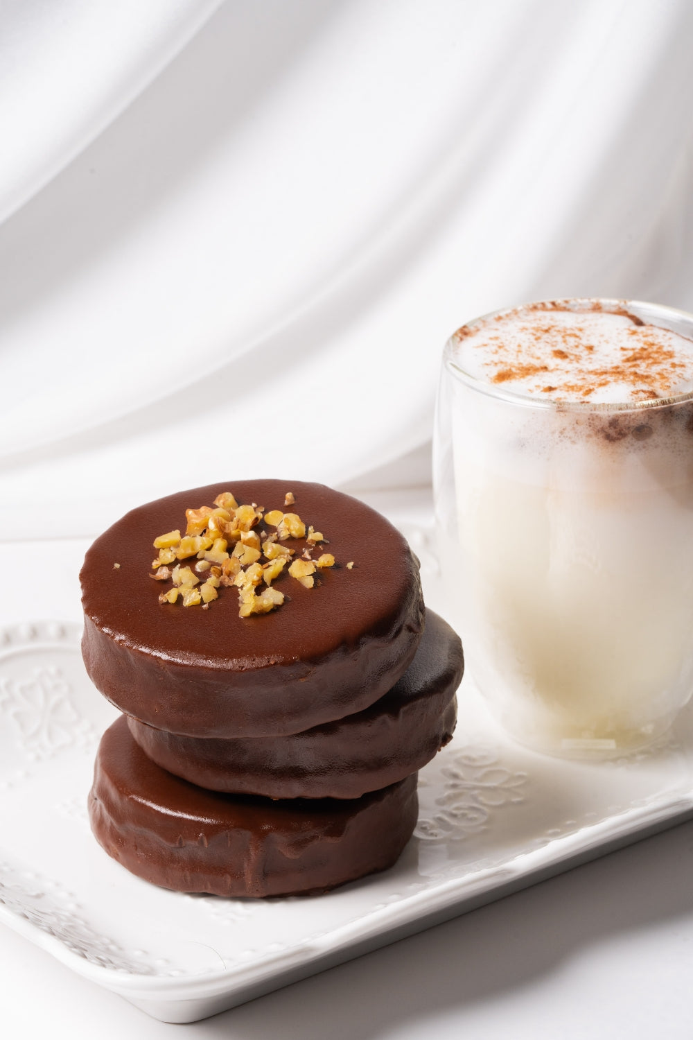 Alfajores de nueces apilados sobre una bandeja. A su lado hay un vaso de leche. 