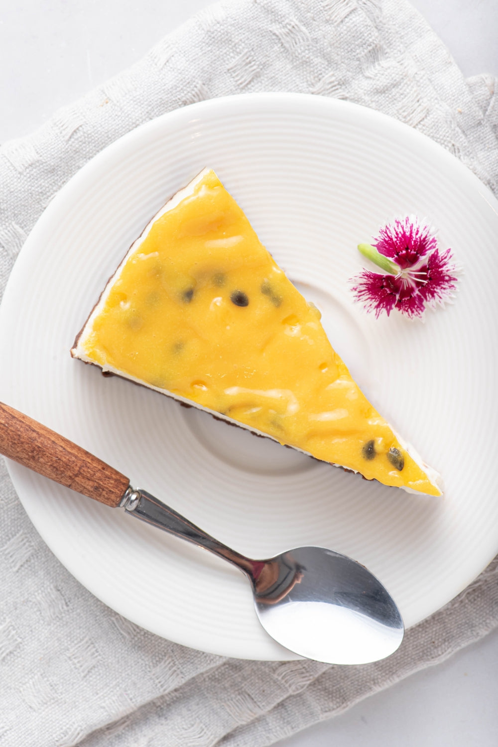 Un pedazo de un cheesecake de maracuya sobre un plato. A su lado se encuentra una cuchara.