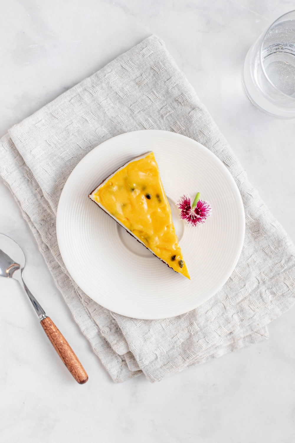 Un pedazo de un cheesecake de maracuya sobre un plato. A su lado se encuentra una cuchara.